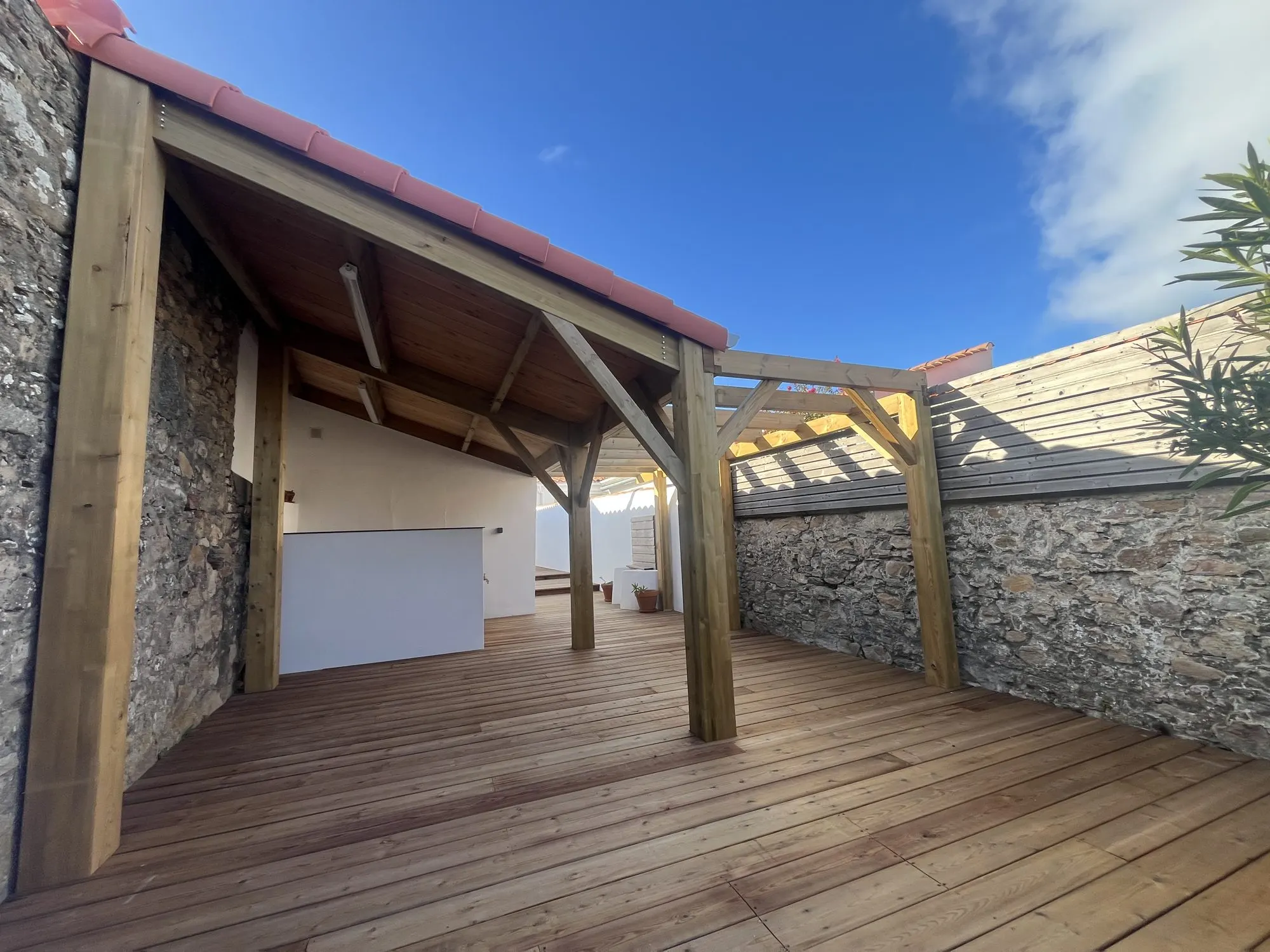 Terrasse en bois couverte, mur en pierre et charpente apparente — maison de vacances à La Chaume