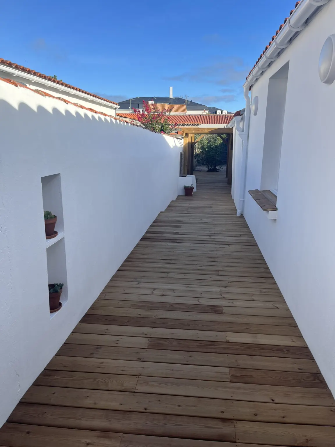 Allée en bois entre les murs blancs vers le jardin — maison de vacances à La Chaume